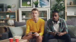 Two friends focus on gaming while relaxing on a couch in a modern living room. — Exactly What Makes W88 A Well-Deserved Gambl
