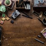 A cluttered artistic workspace with paints, brushes, and tools on a wooden table